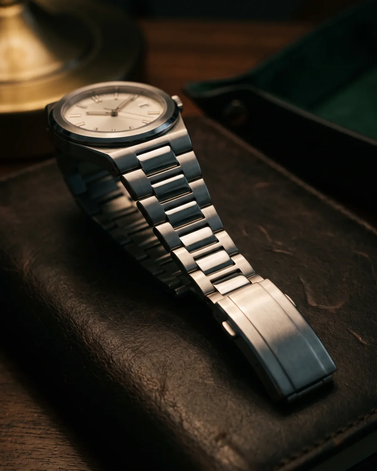 A Nautilus bracelet on its side on a dark desk: brushed outer links, polished centre links, the fold-over clasp, and two spare links.