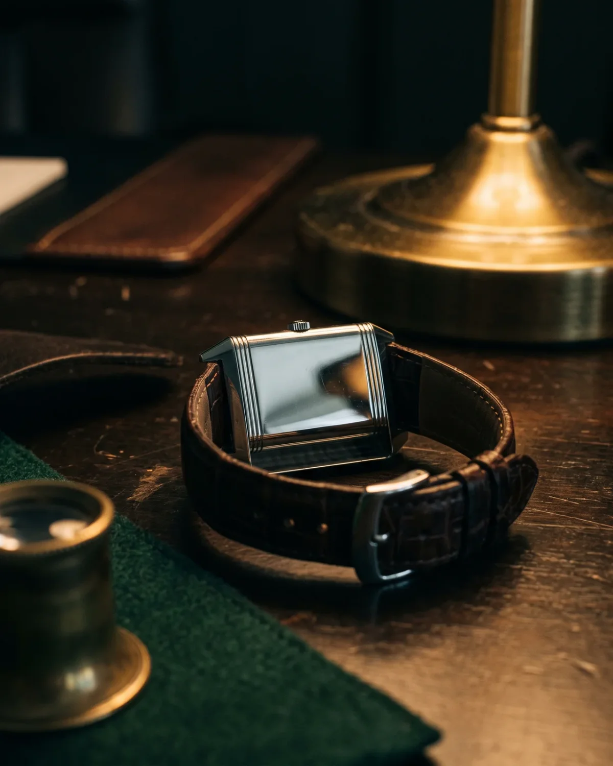 The solid back of a rectangular reversible watch with plain brushed steel, set beside its fitted presentation box and a folded warranty booklet on a dark surface.