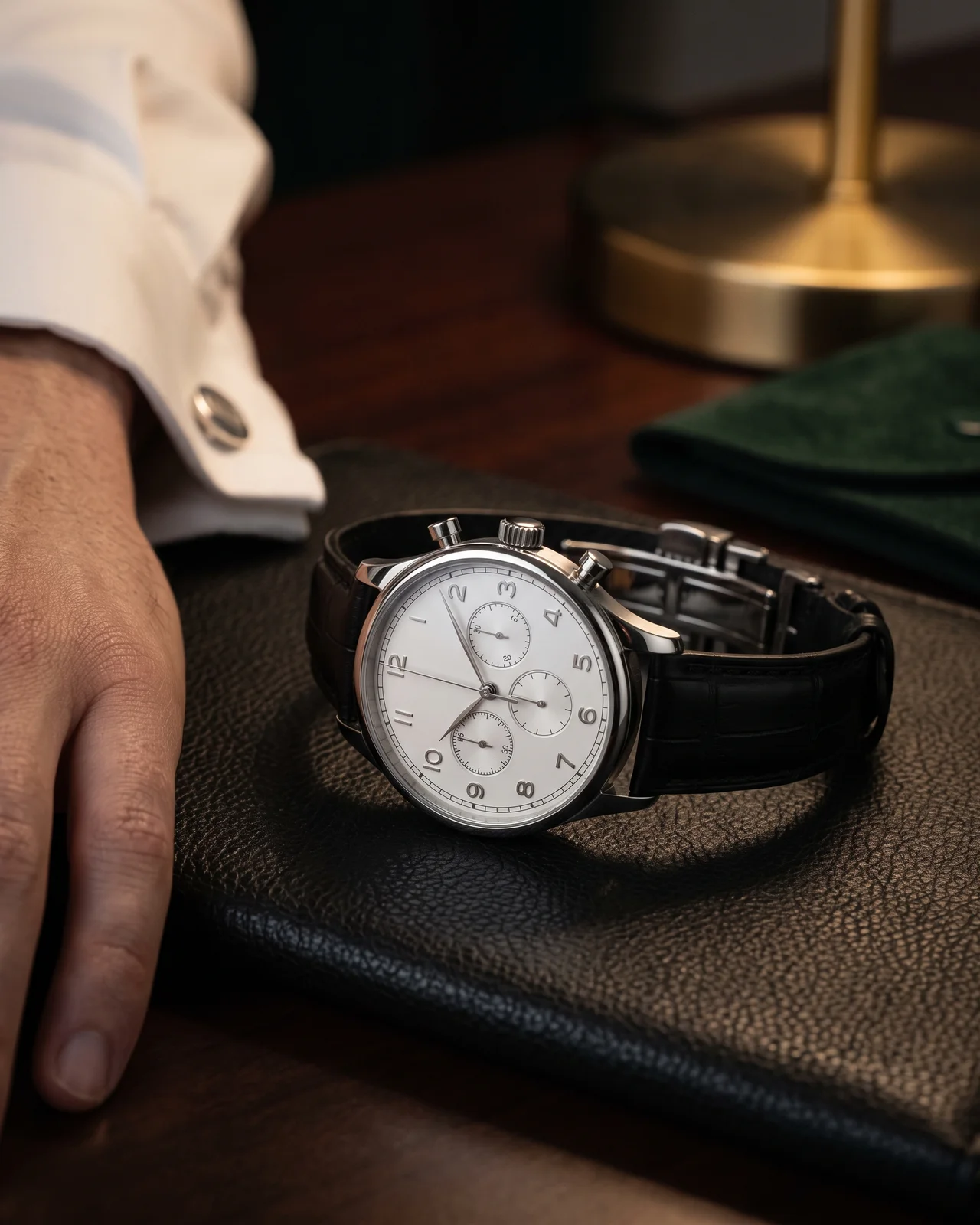 A silver-dial Portugieser Chronograph with blued leaf hands and applied Arabic numerals, on a dark alligator strap, on dark felt under a brass lamp.