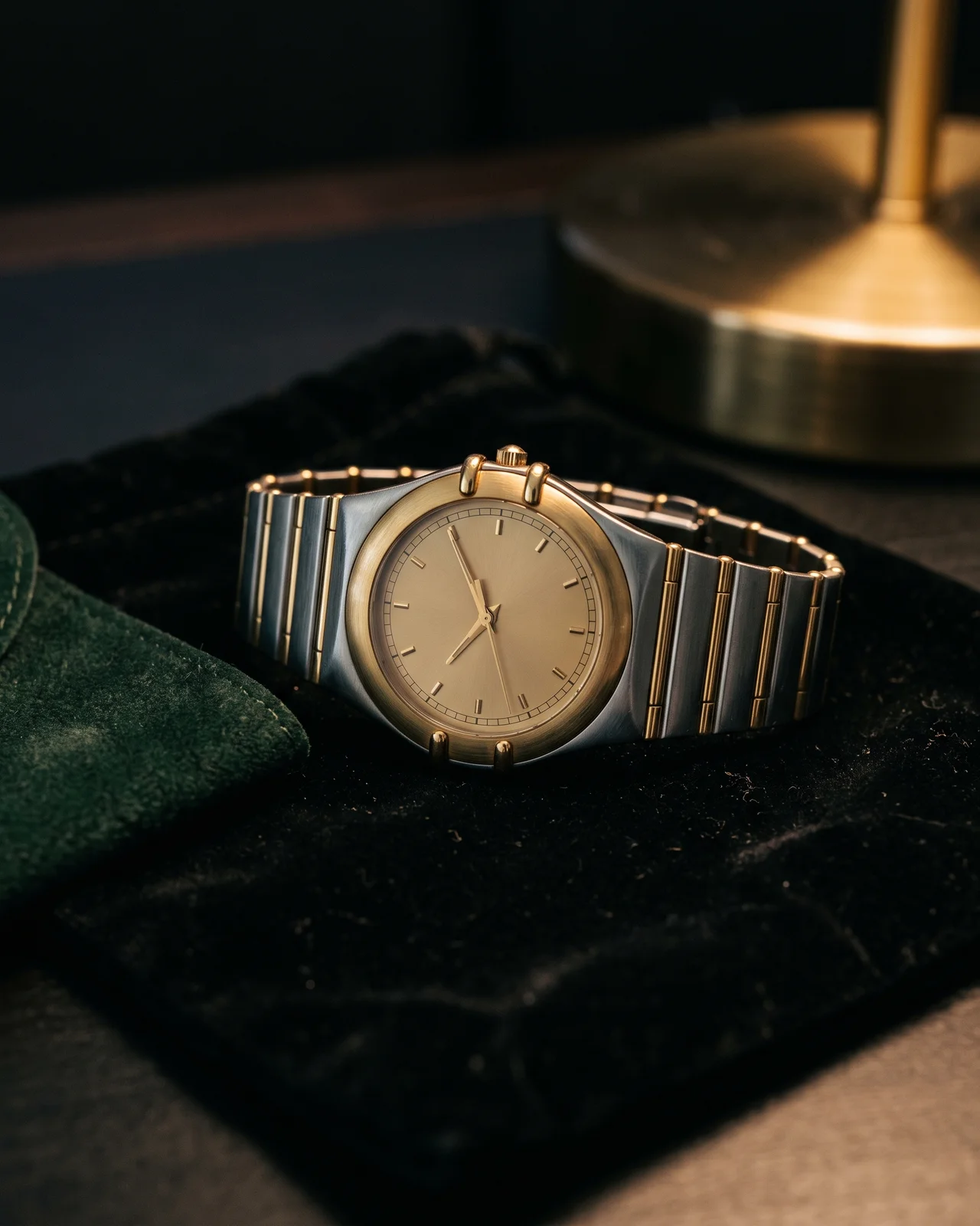 A two-tone Constellation Manhattan with the four claws at the sides of the crystal and an integrated bracelet, on dark felt under a brass lamp.