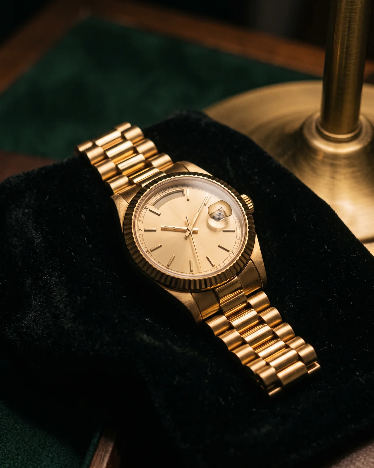 A yellow gold Day-Date with a champagne dial on a President bracelet, on dark felt under a brass lamp.